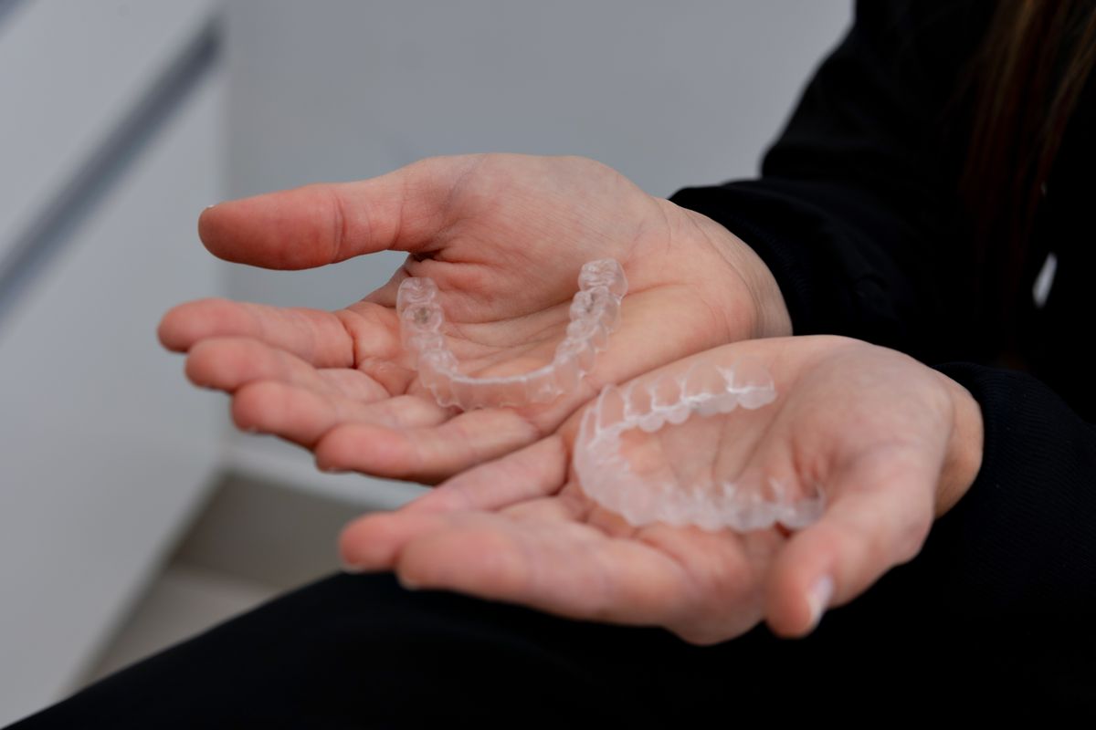 Hands holding a pair of clear dental aligners